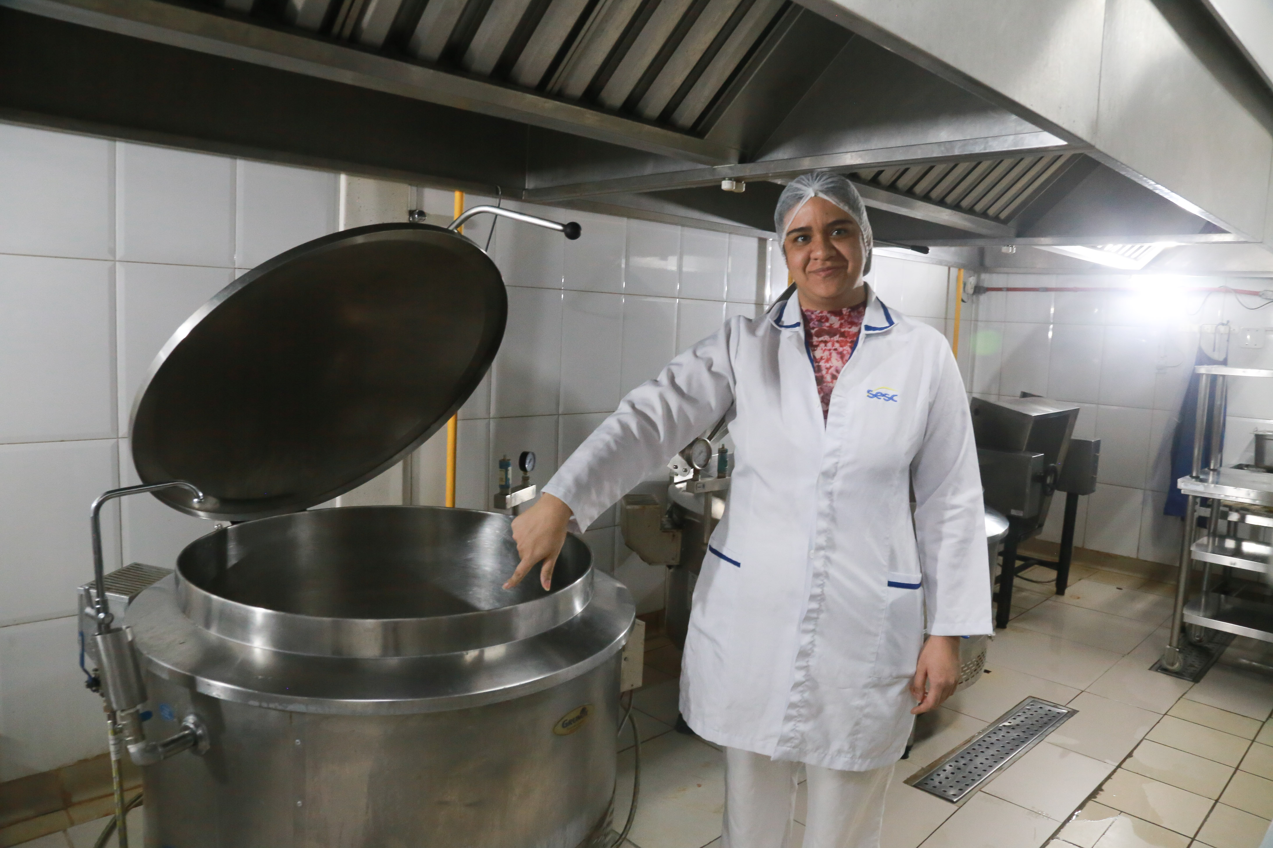 mulher ao lado de um panelão industrial de preparo de sopa